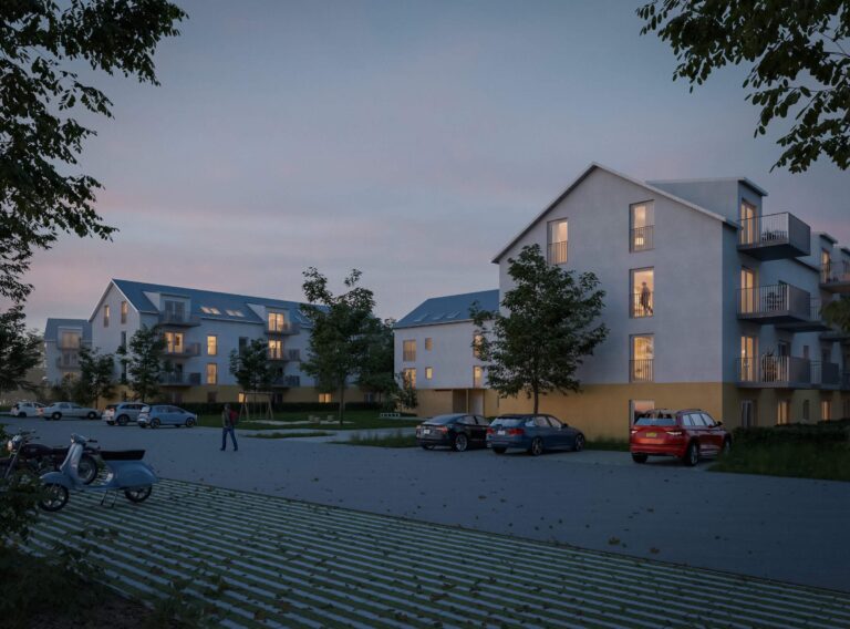 Visualisierung einer modernen Wohnanlage in der Abenddämmerung. Mehrere drei- bis vierstöckige Gebäude mit hellen Fassaden, gelb abgesetzten Erdgeschosszonen und blauen Satteldächern gruppieren sich um einen gepflasterten Außenbereich mit Parkplätzen. In den Fenstern brennt warmes Licht, und im Vordergrund ist eine gepflasterte Fläche mit Rasenfugen sowie ein geparkter Motorroller zu sehen.