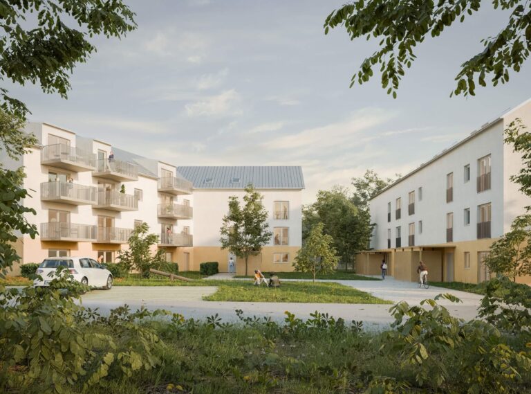Hell erleuchtete Außenansicht der Wohngebäude bei Tageslicht. Die Architektur zeigt weiße Fassaden mit Balkonen und einer markanten ockerfarbenen Sockelzone. Im grünen Innenhof befinden sich eine Rasenfläche mit einer Wippe, junge Bäume und Bewohner, die auf der Wiese sitzen. Ein weißer Pkw parkt am linken Bildrand, rechts führt ein Weg an einem flachen Nebengebäude vorbei.